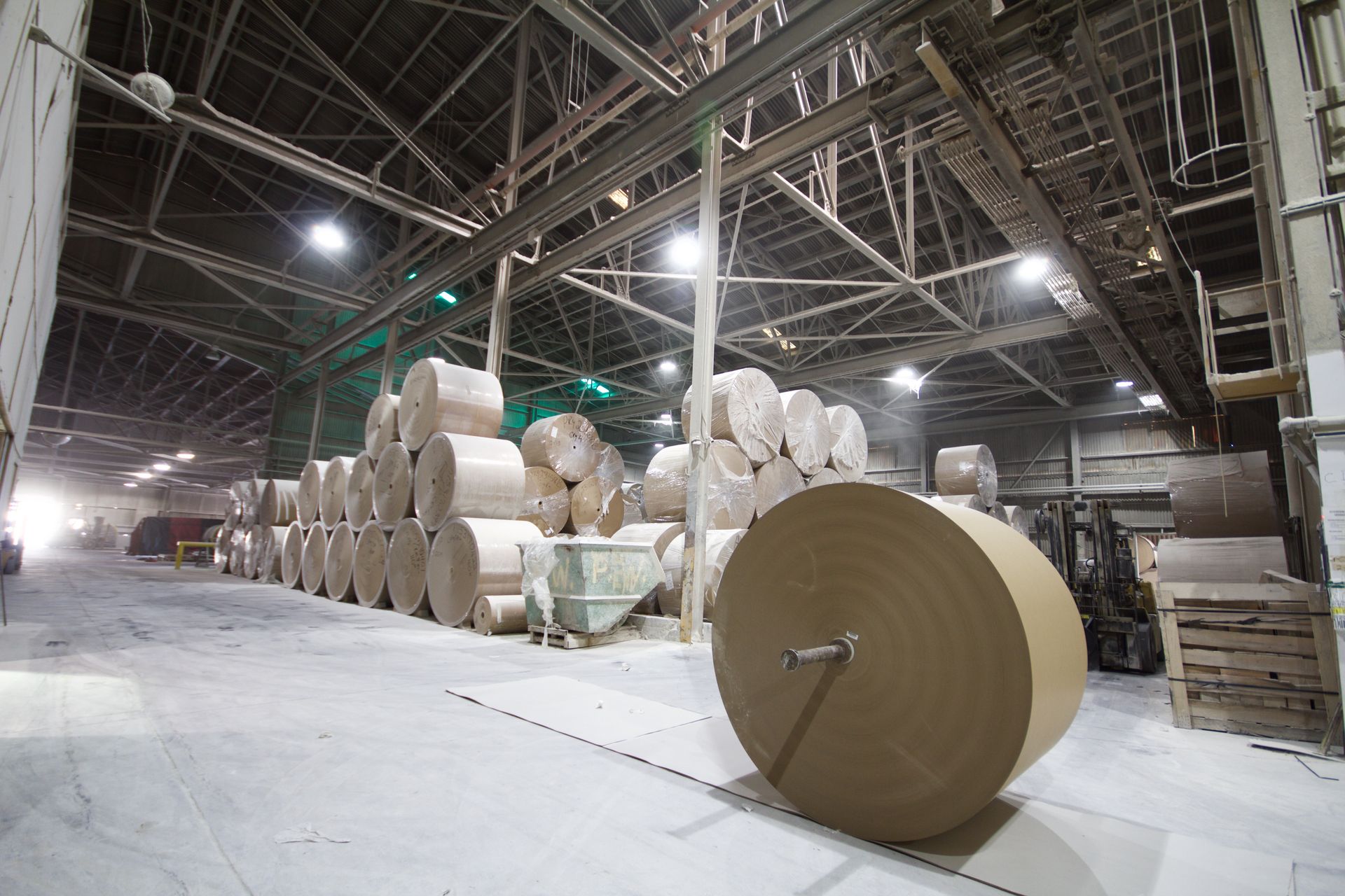 Large industrial warehouse with stacked rolls of paper and a giant paper roll in the foreground.
