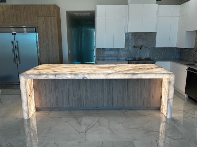 Modern kitchen with a marble waterfall island, stainless steel fridge, and white cabinets
