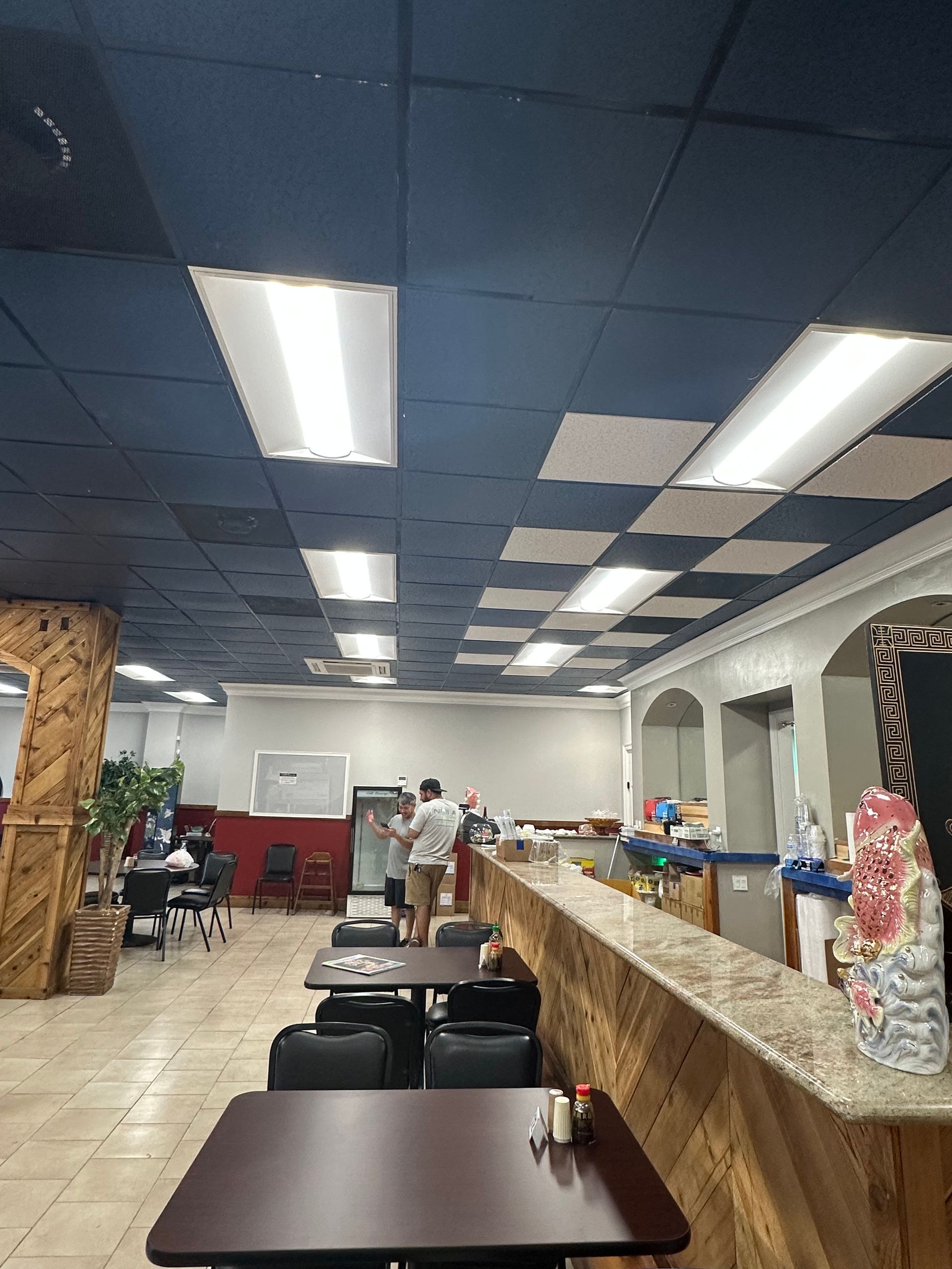 Restaurant interior with long counter, tiled floor, ceiling lights, and workers near the back wall