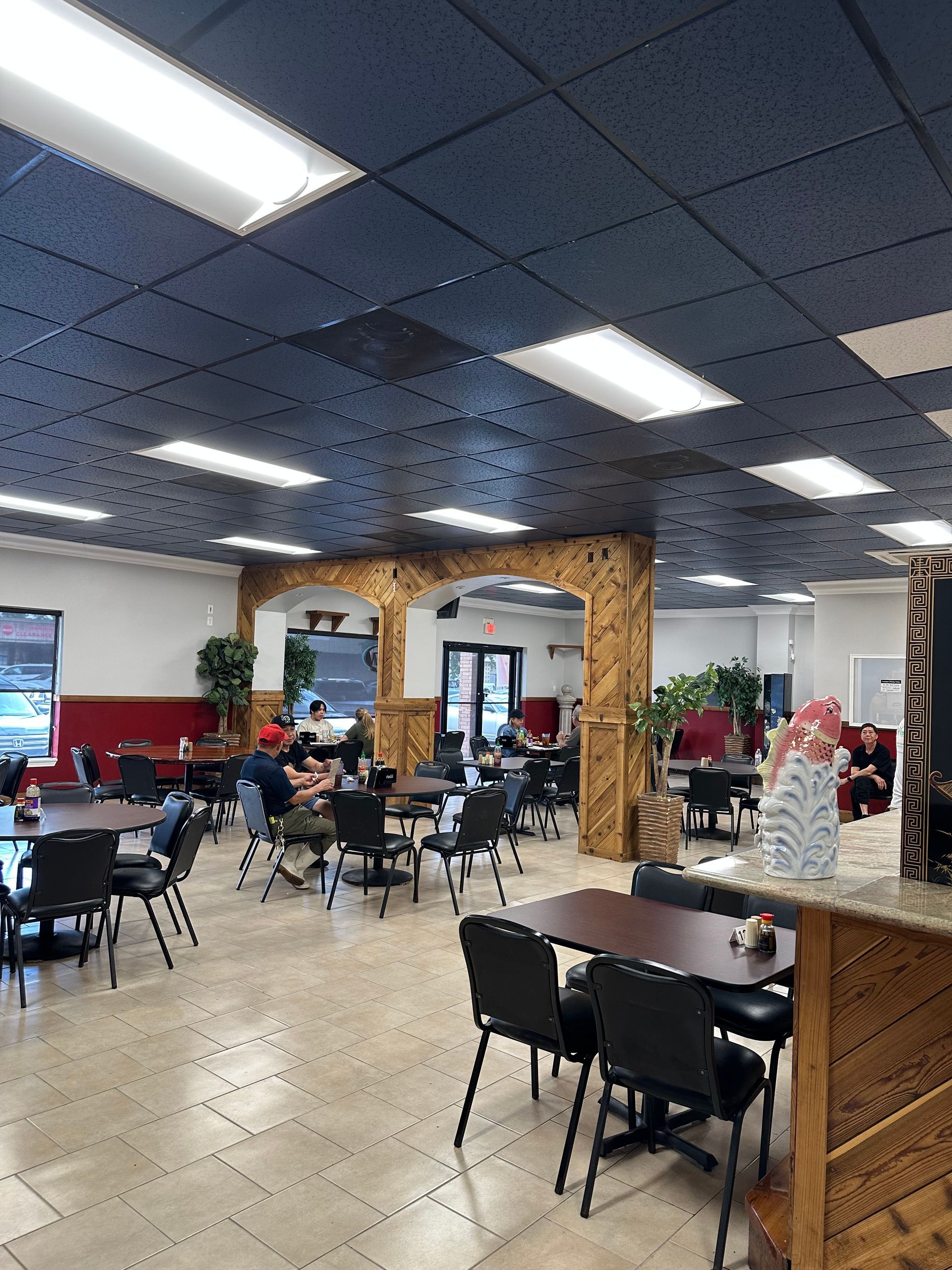 Spacious cafeteria with tables, black chairs, tiled floor, and blue ceiling lights; few people seated.