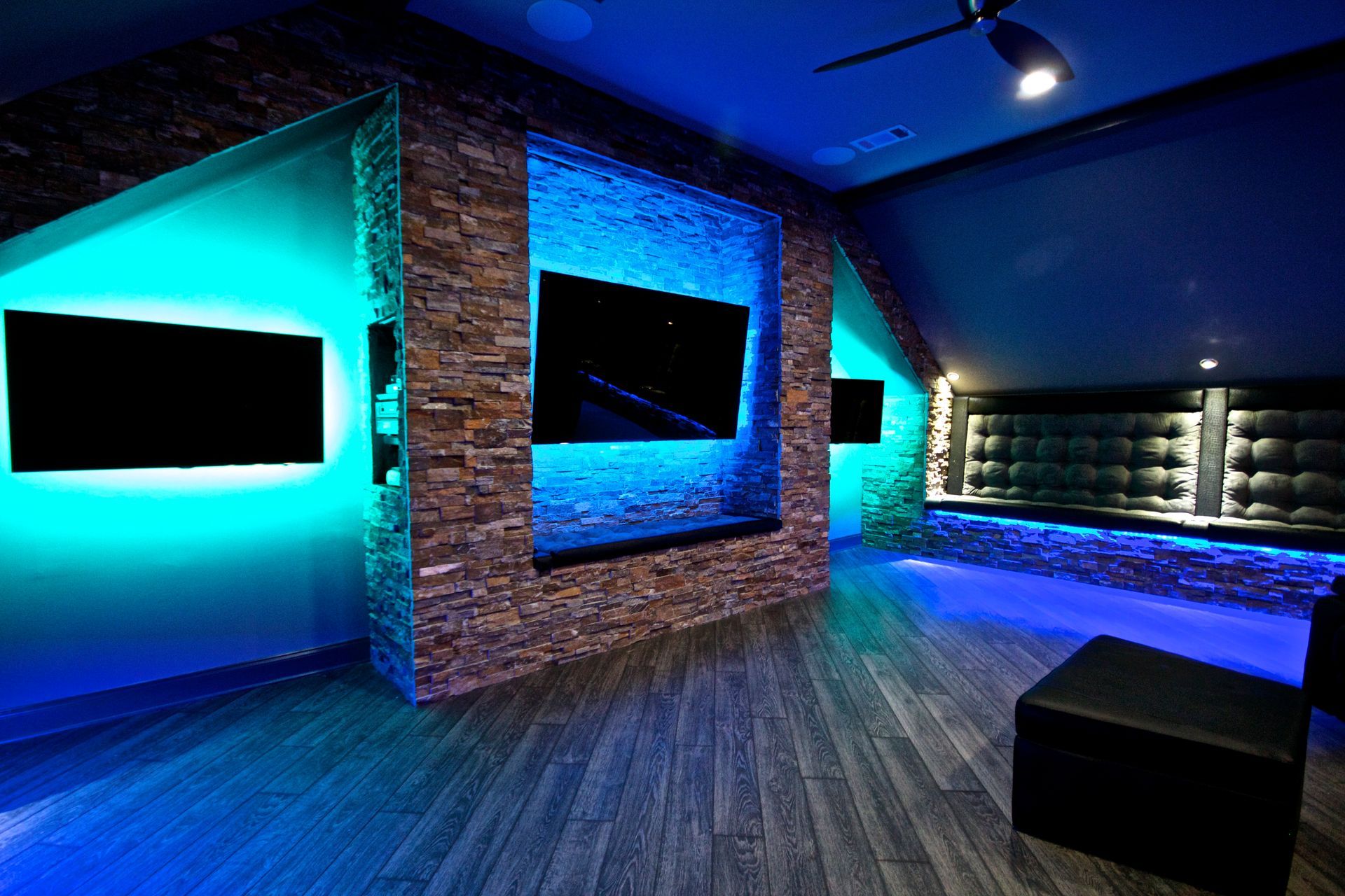 Modern media room with blue LED lighting, wall-mounted screens, and brick and wood finishes