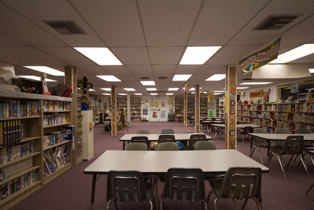 Library reading room with tables, chairs, and bookshelves under bright fluorescent lights