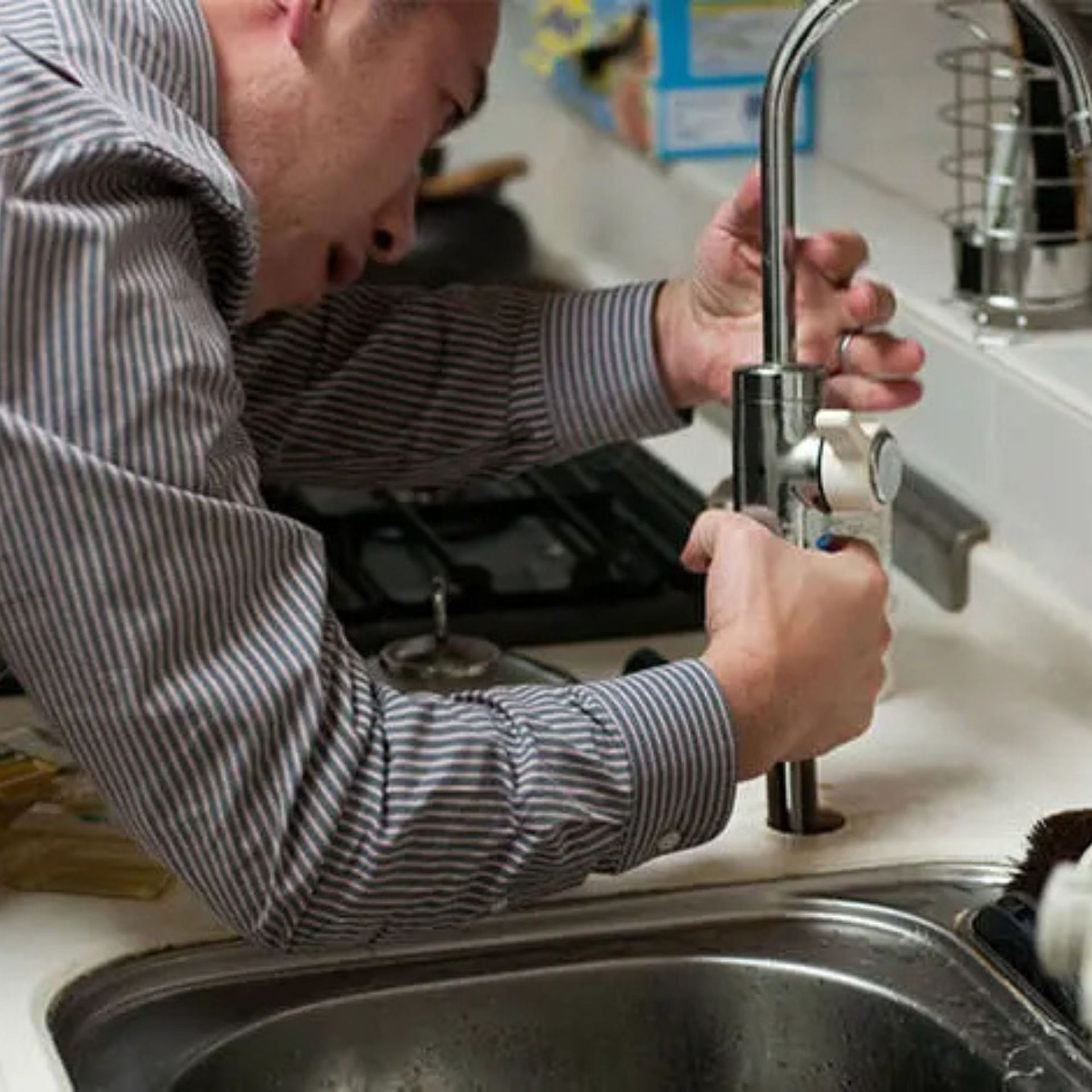 JM Plumbing Inc | A man is fixing a faucet in a kitchen sink.