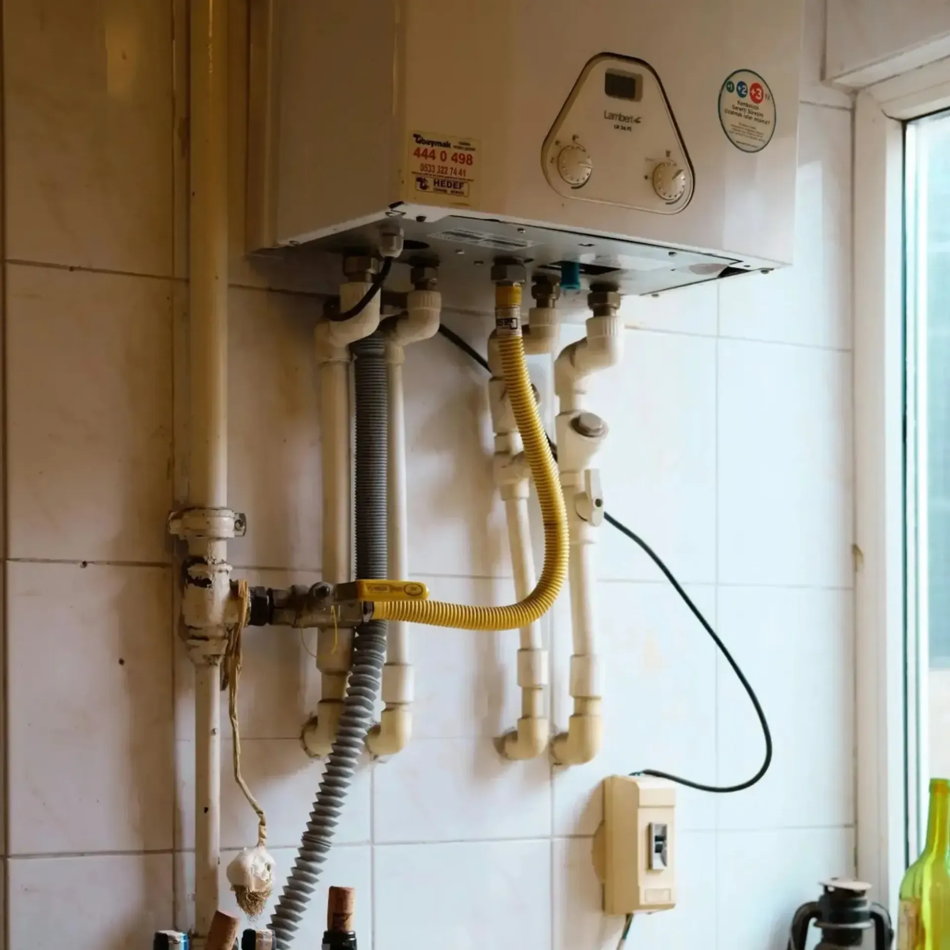 JM Plumbing Inc | A white water heater is mounted to a white tiled wall