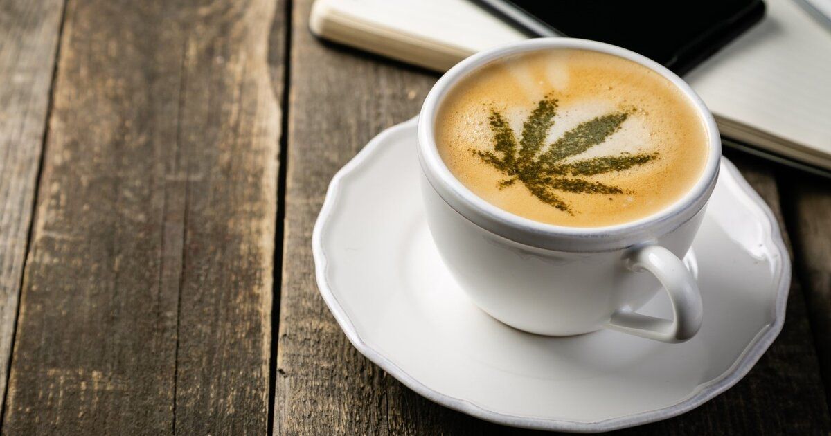 Cup of coffee with cannabis leaf design on a saucer, on a wooden table.