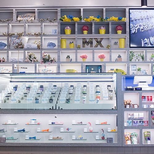 A brightly lit dispensary with various products in display cases, shelves with floral arrangements and a digital menu.