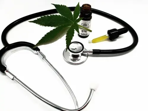 Stethoscope with CBD oil bottle, dropper, and cannabis leaf, on white.