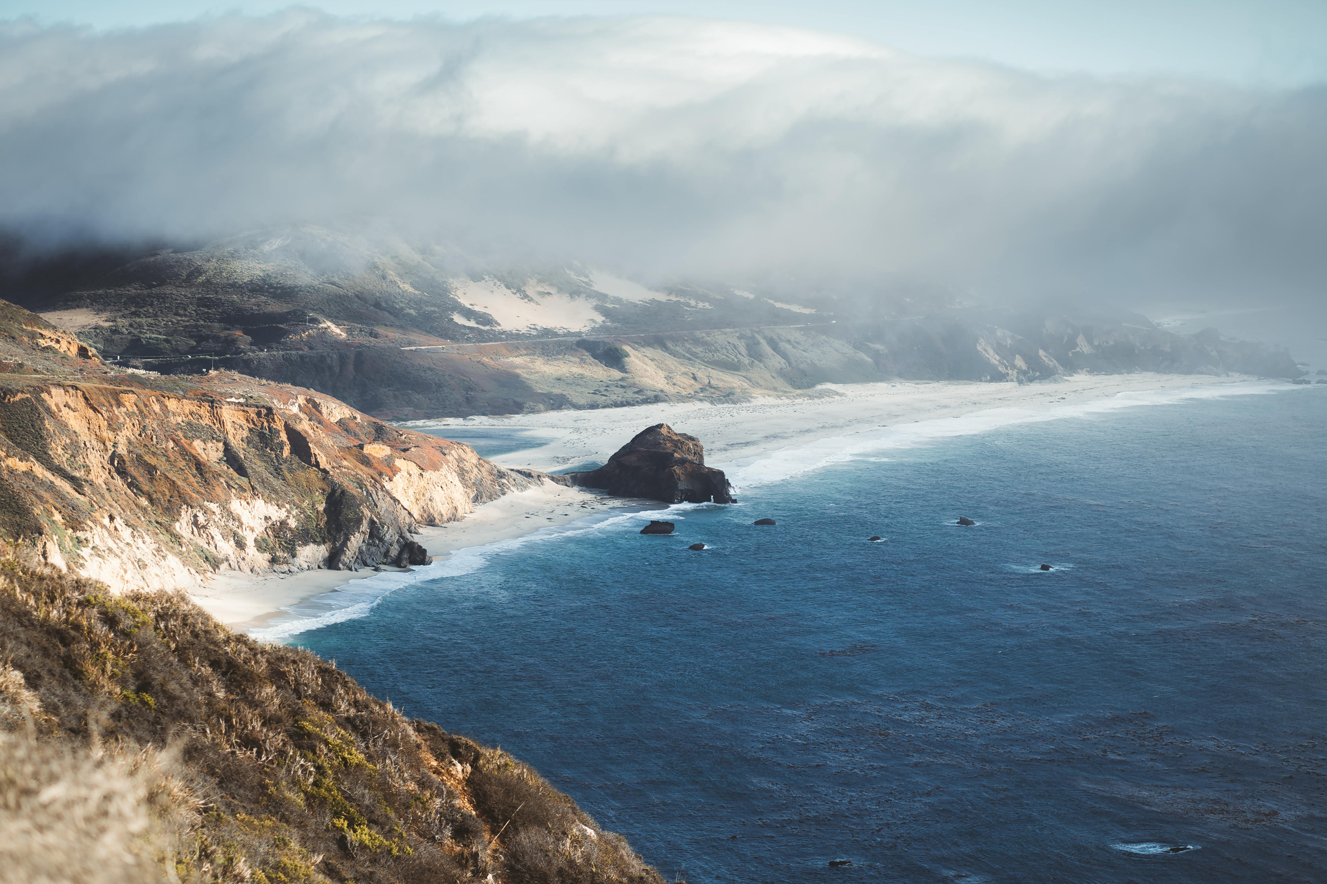 Coastal view with cliffs, sandy beach, and ocean under a cloudy sky.