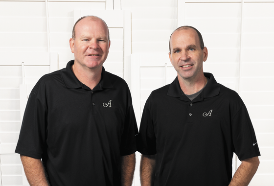 Artisan Shutter founders on background of plantation shutters