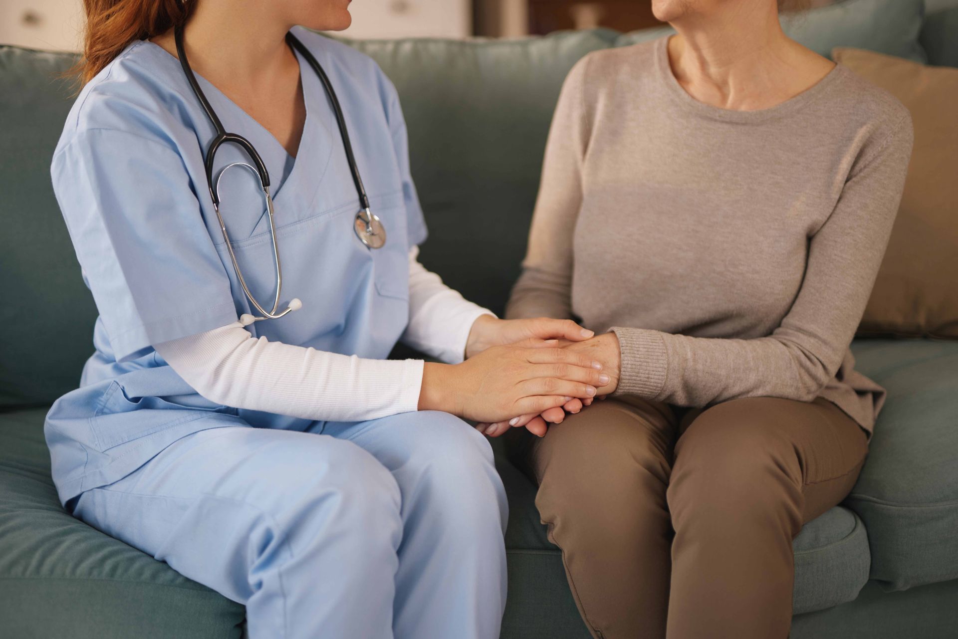 Nurse in blue scrubs holding hands with a patient on a couch. Nurse in blue scrubs holding hands with a patient on a couch.