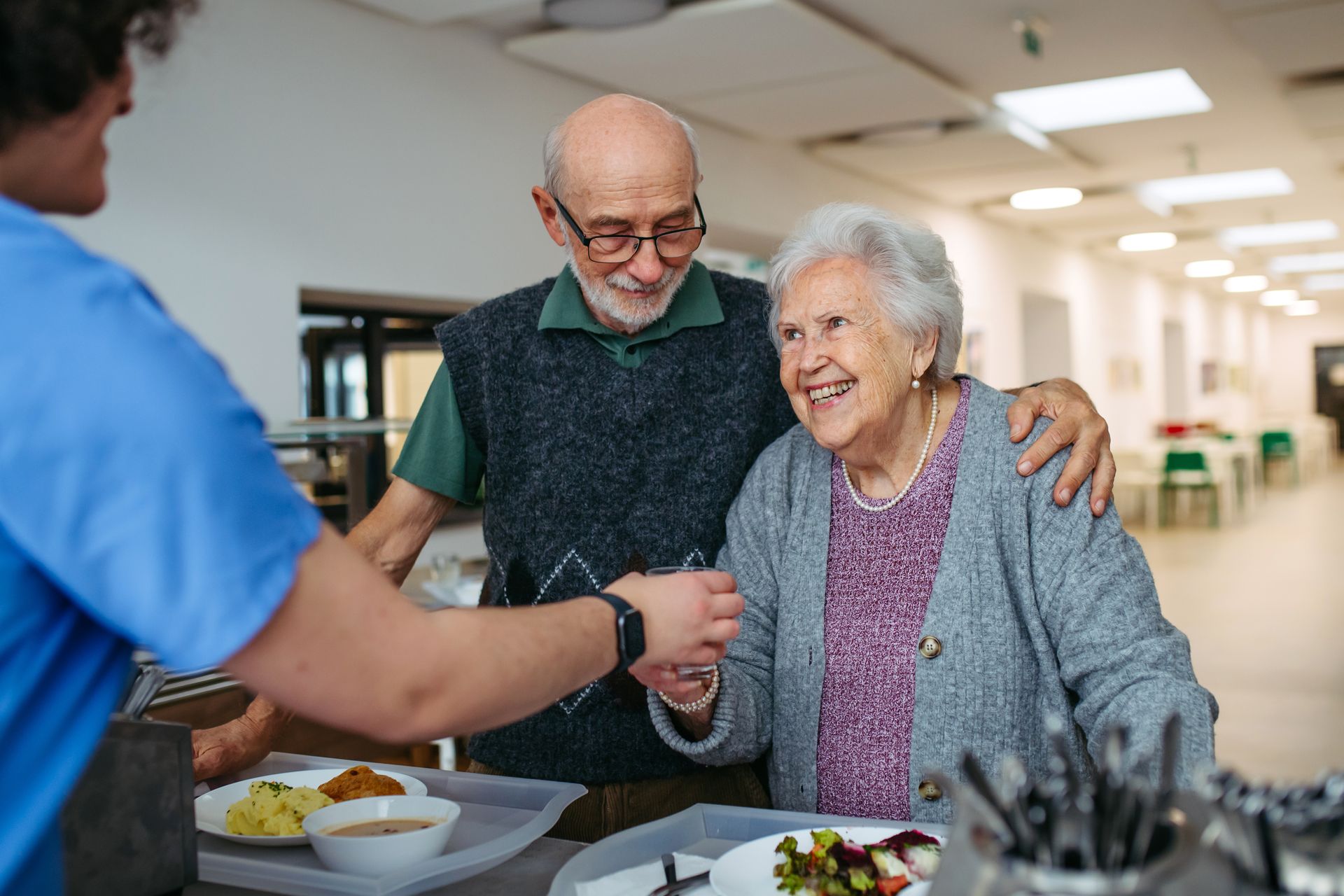 Smiling senior couple receiving a warm meal from a caregiver in an assisted living community setting
