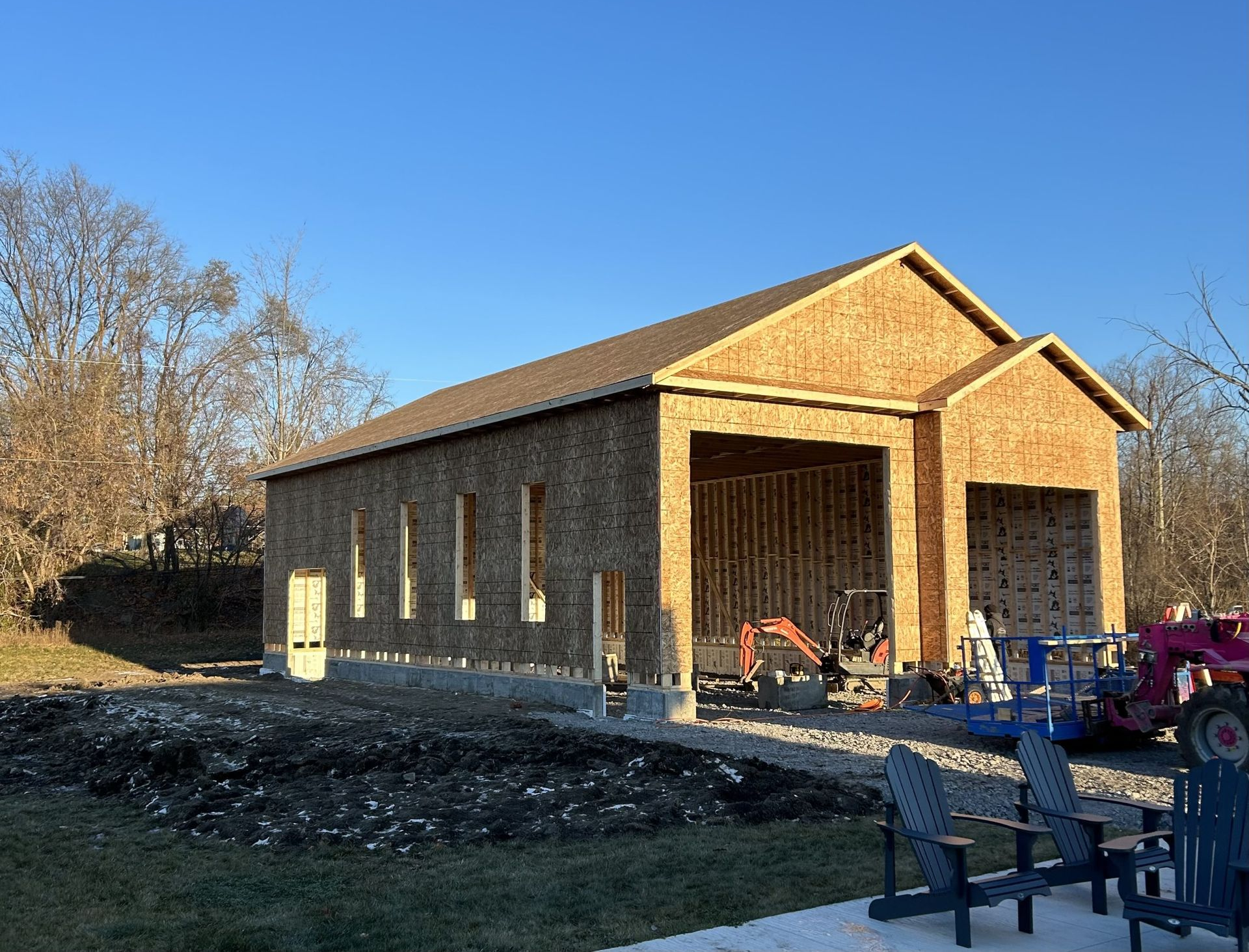 Extérieur d'un garage à ossature bois partiellement aménagé, avec des travées ouvertes et du matériel de construction