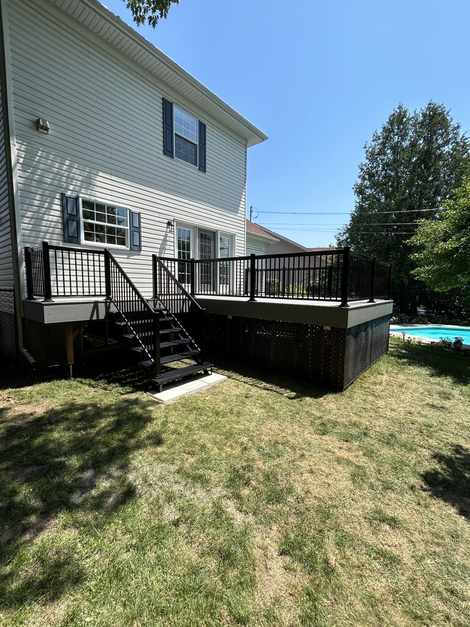 Terrasse arrière avec rambarde noire, escalier et piscine hors sol à côté d'une maison blanche.