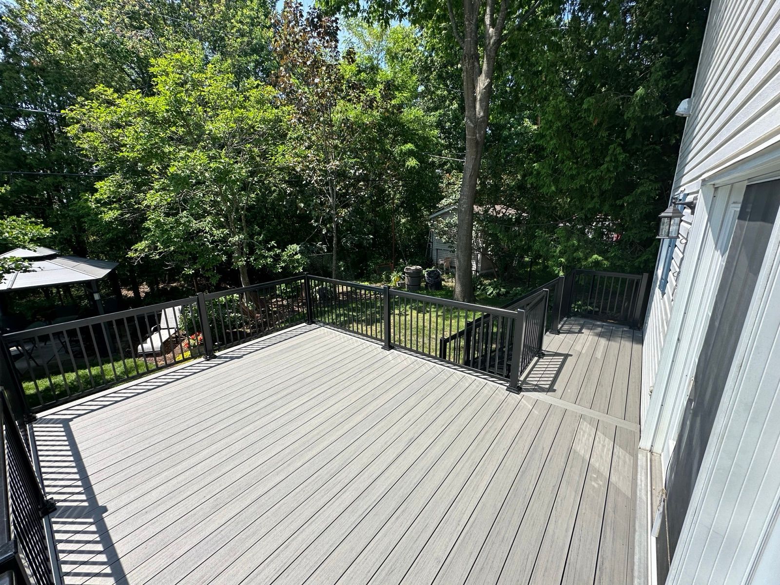 Terrasse arrière avec sol gris clair, rambarde noire et arbres dans le jardin au-delà