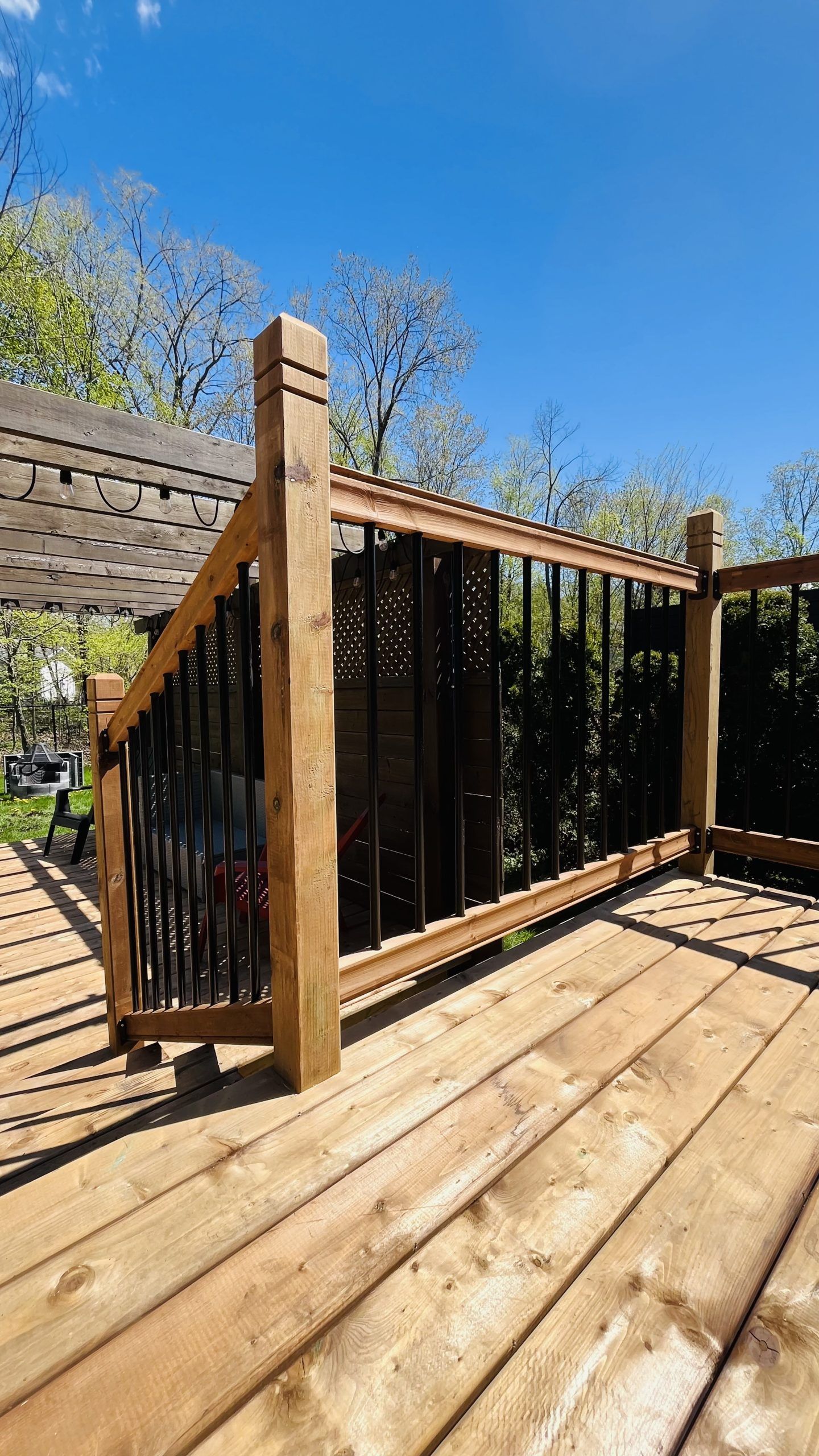 Terrasse en bois avec une rambarde noire et un ciel bleu au-dessus, vue depuis un coin