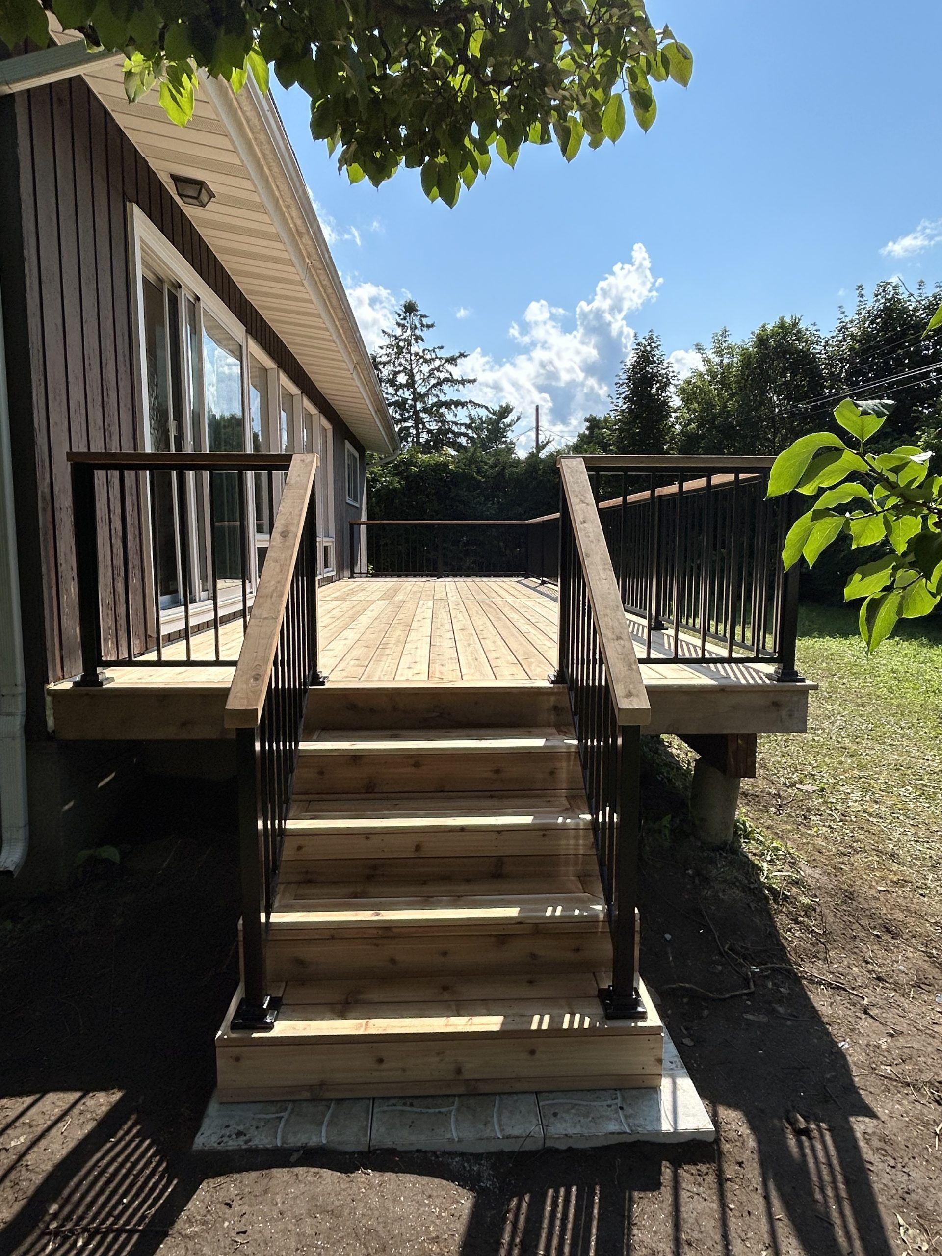 Terrasse en bois dans la cour arrière avec marches, rambardes et rampe ensoleillée à côté d'une maison
