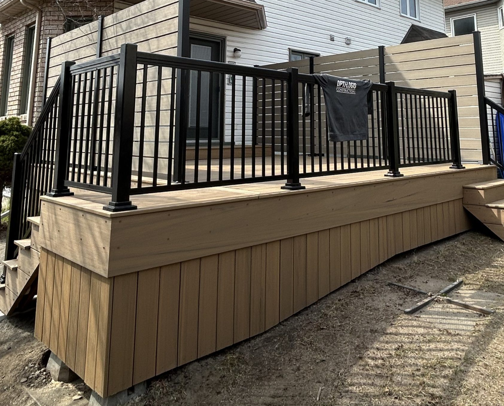 Plateforme en bois avec rambarde en métal noir à côté d'une maison et d'un escalier extérieur