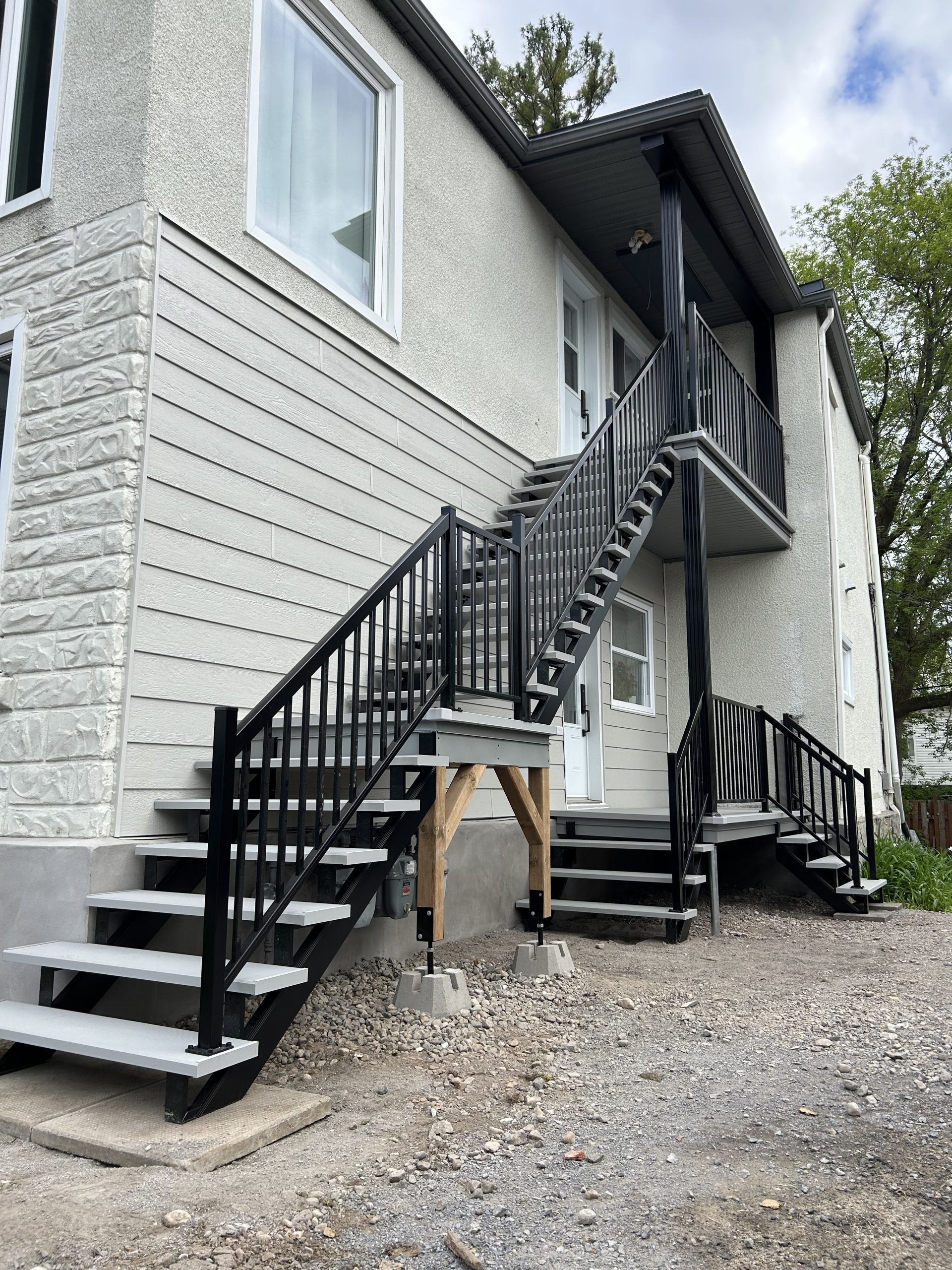 Escaliers extérieurs et balcons en métal noir sur une maison à façade blanche, construite sur du gravier.