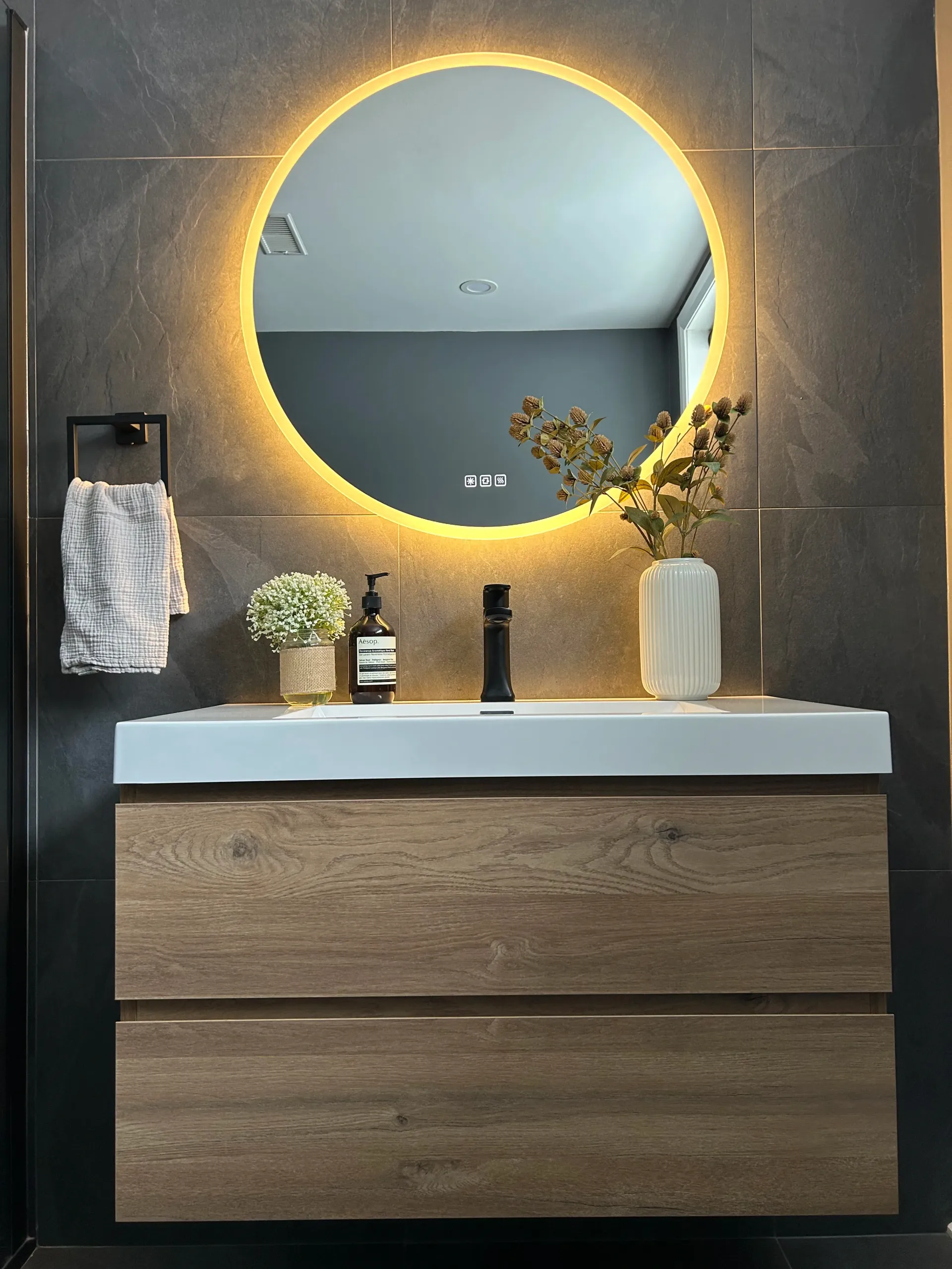 Meuble-lavabo moderne avec miroir rond rétroéclairé, armoire en bois, lavabo et porte-serviettes mural.