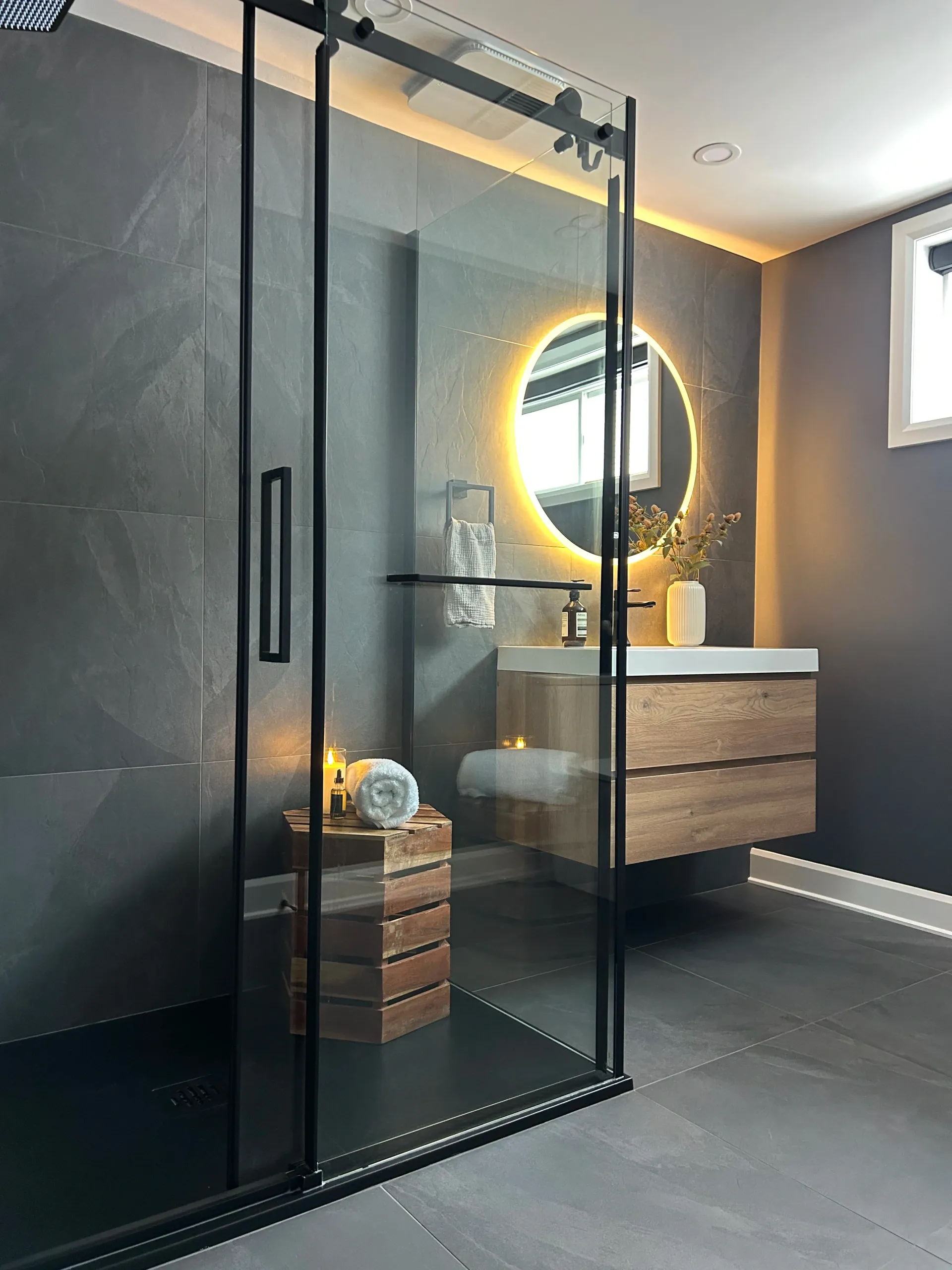 Salle de bains moderne avec douche en verre, meuble-lavabo mural et miroir rond éclairé
