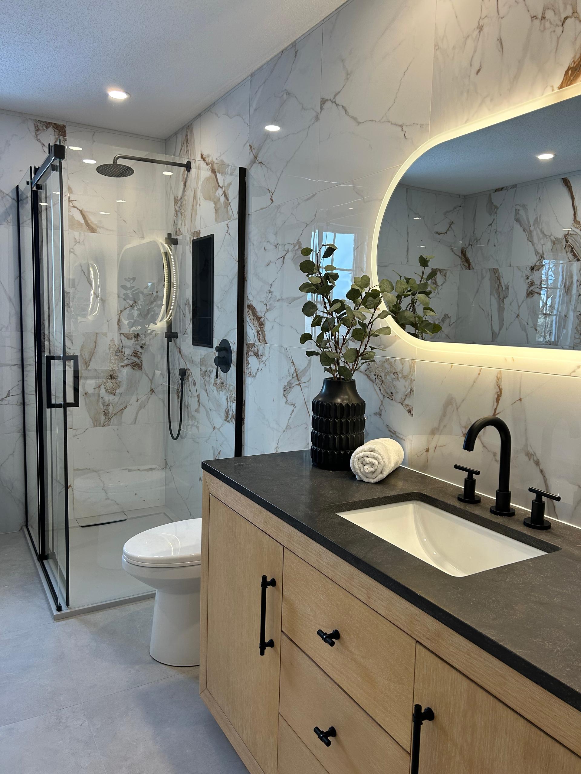 Salle de bains moderne avec douche en marbre, robinetterie noire et meuble-lavabo en bois avec vasque.