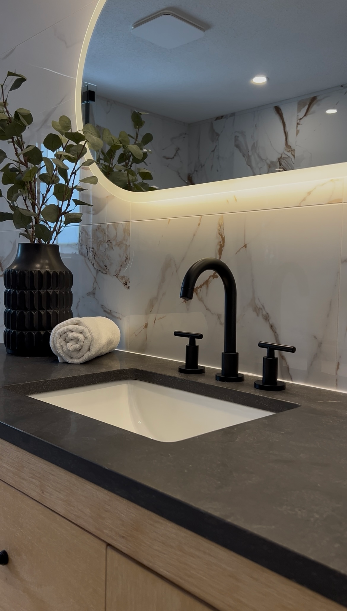 Meuble-lavabo moderne avec robinet noir, lavabo blanc, miroir et éclairage doux sous le meuble.