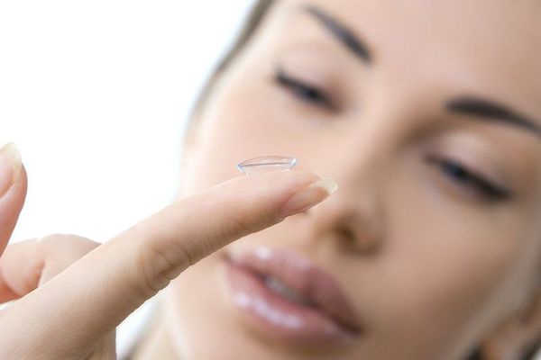 A woman is putting a contact lens on her finger.