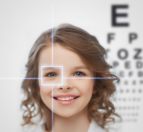 A young girl is smiling in front of an eye chart