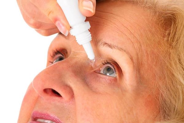 A woman is applying eye drops to her eye.