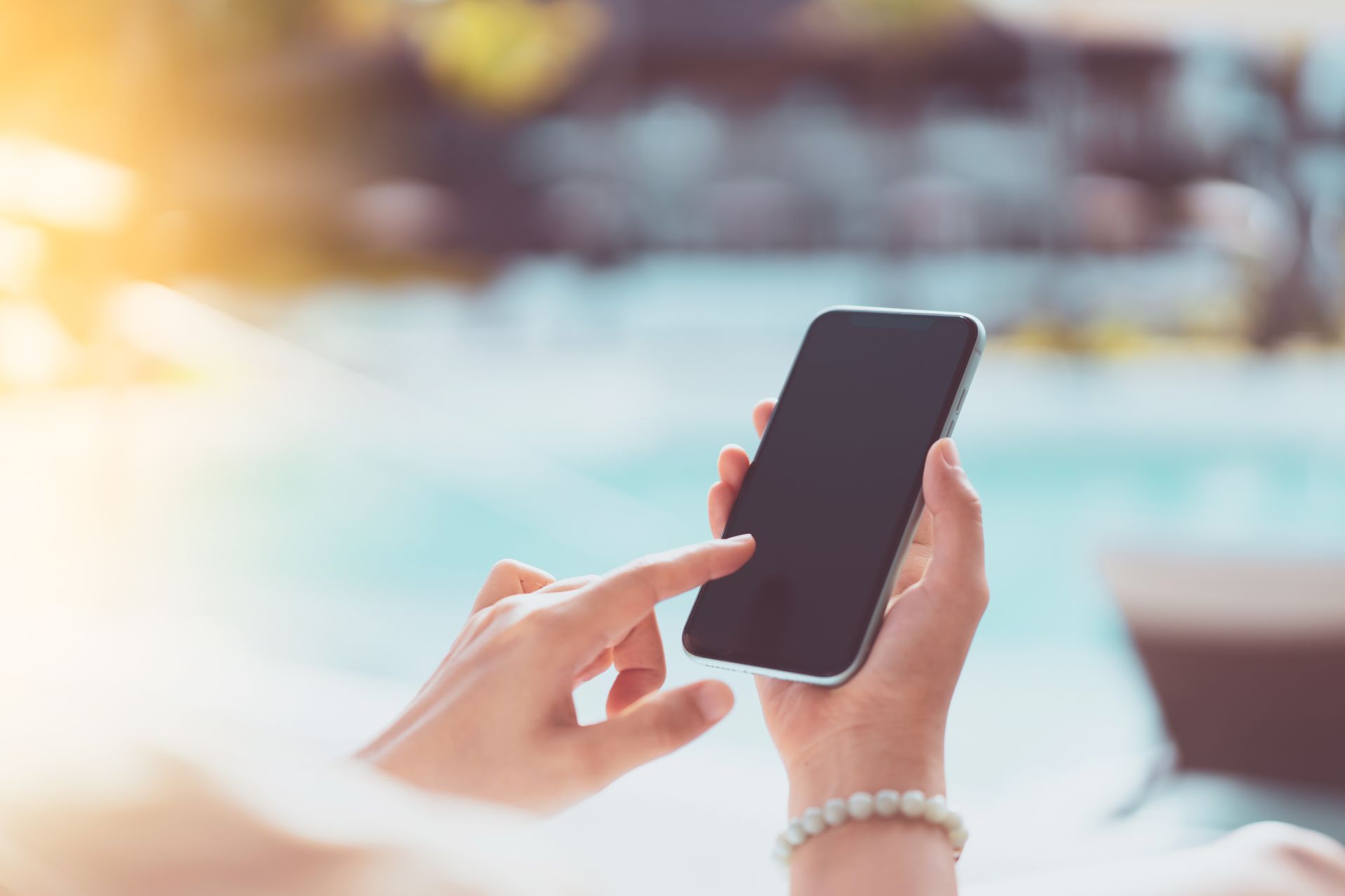 A woman is using a cell phone in front of a pool.