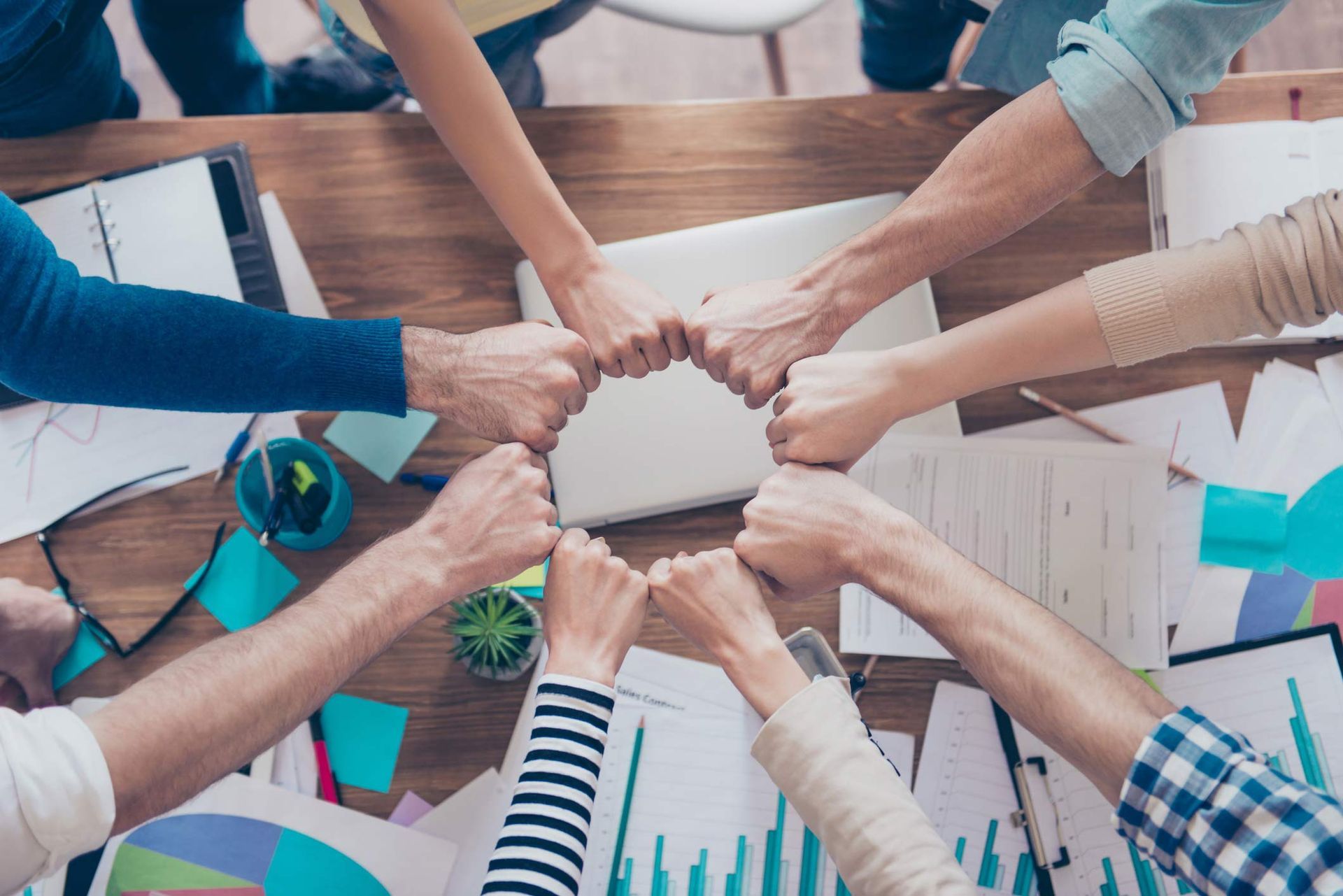 Close Up Cropped Photo Of Partners Putting Their Fists Together In A Circle On Top Of The Table With Work Stuff — Placida, FL — Accounting 4 Profitability LLC Close Up Cropped Photo Of Partners Putting Their Fists Together In A Circle On Top Of The Table With Work Stuff — Placida, FL — Accounting 4 Profitability LLC