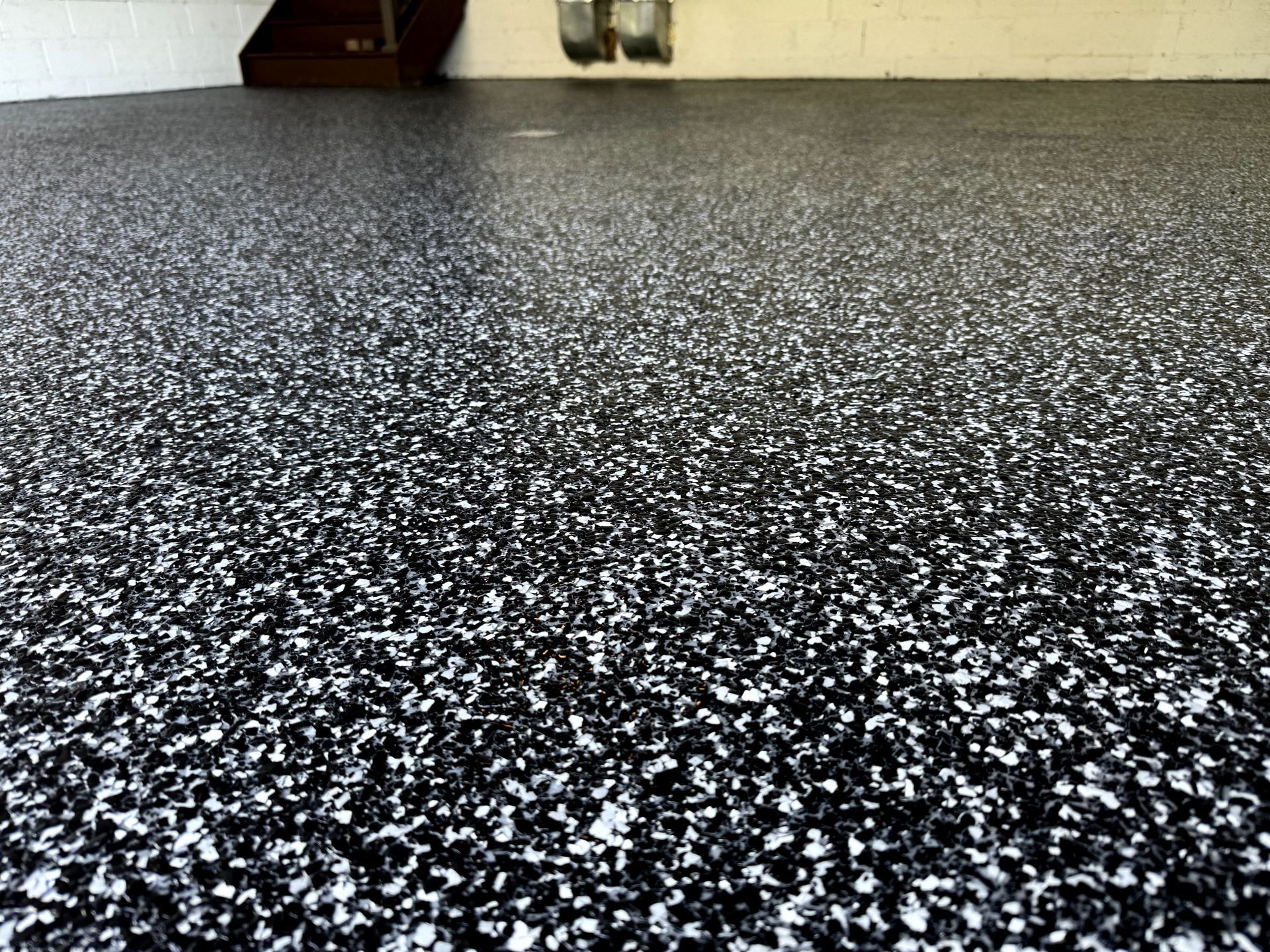 Black-and-white speckled floor carpet in a room corner near a wall and furniture.