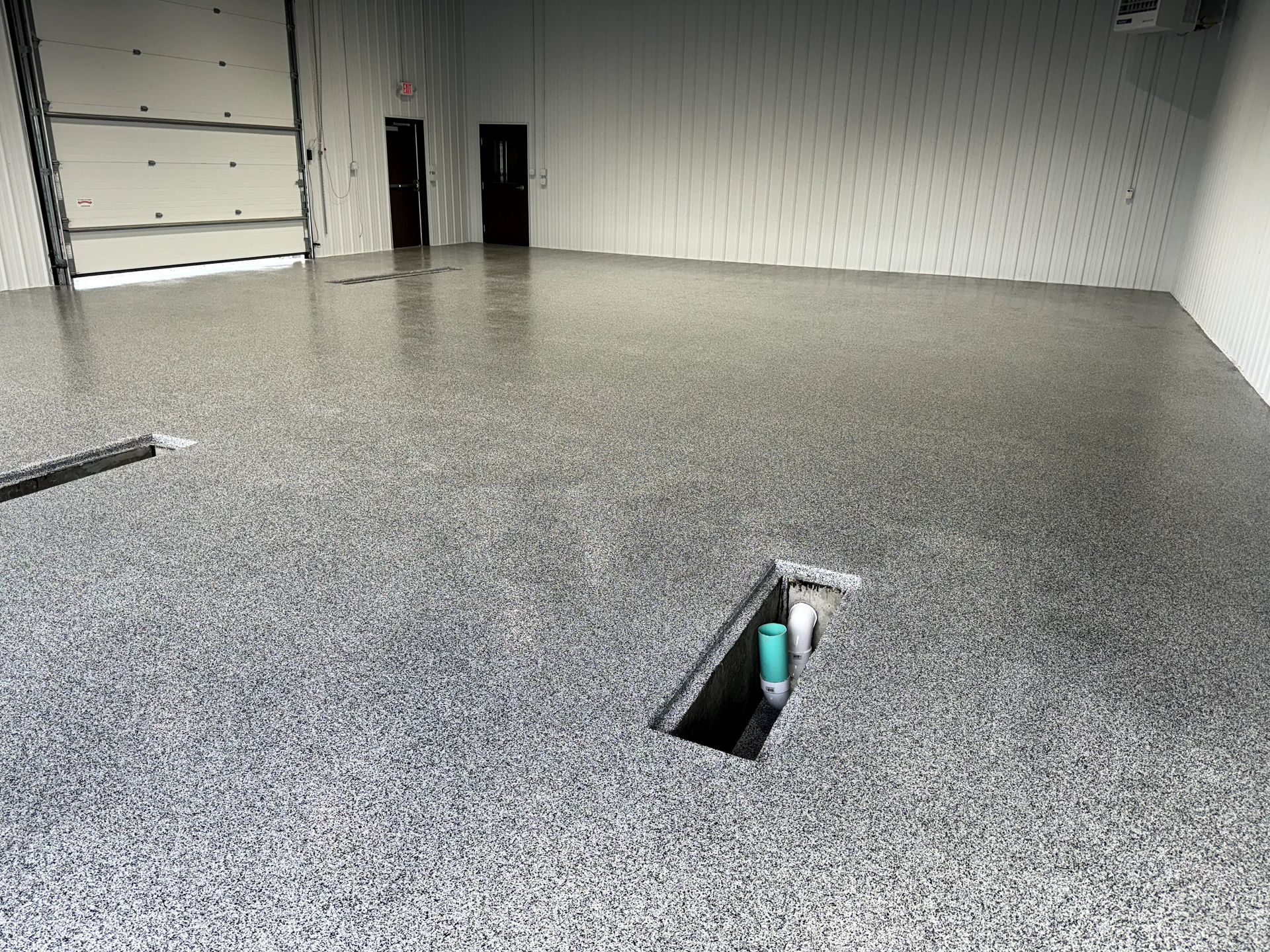 Empty industrial garage with speckled gray floor and open floor drain, viewed from inside.