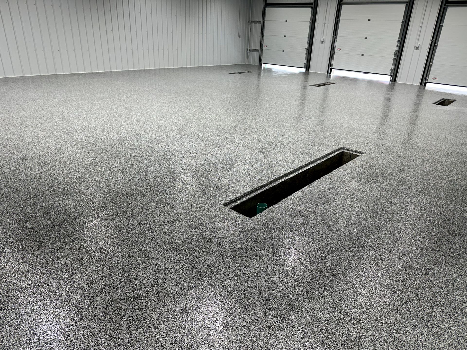 Empty industrial room with speckled gray floor and a rectangular floor drain near the center.