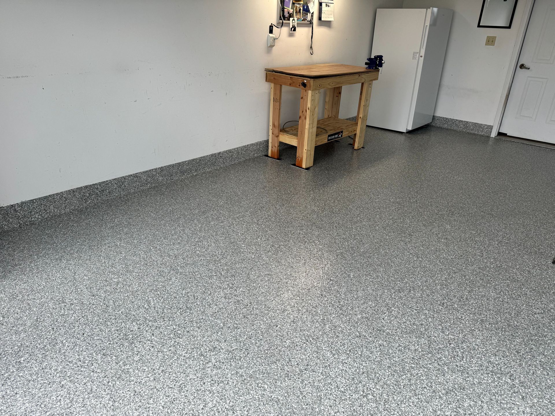 Empty garage with a wooden workbench, white cabinet, and speckled gray floor.