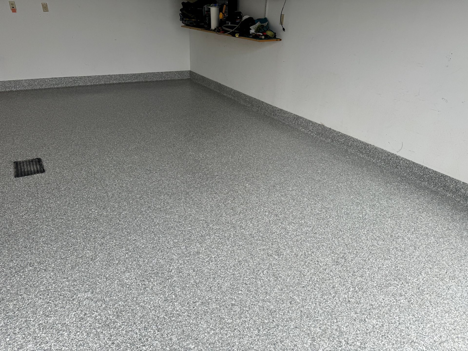 Empty gray-floored room with white walls and a small shelf in the back corner