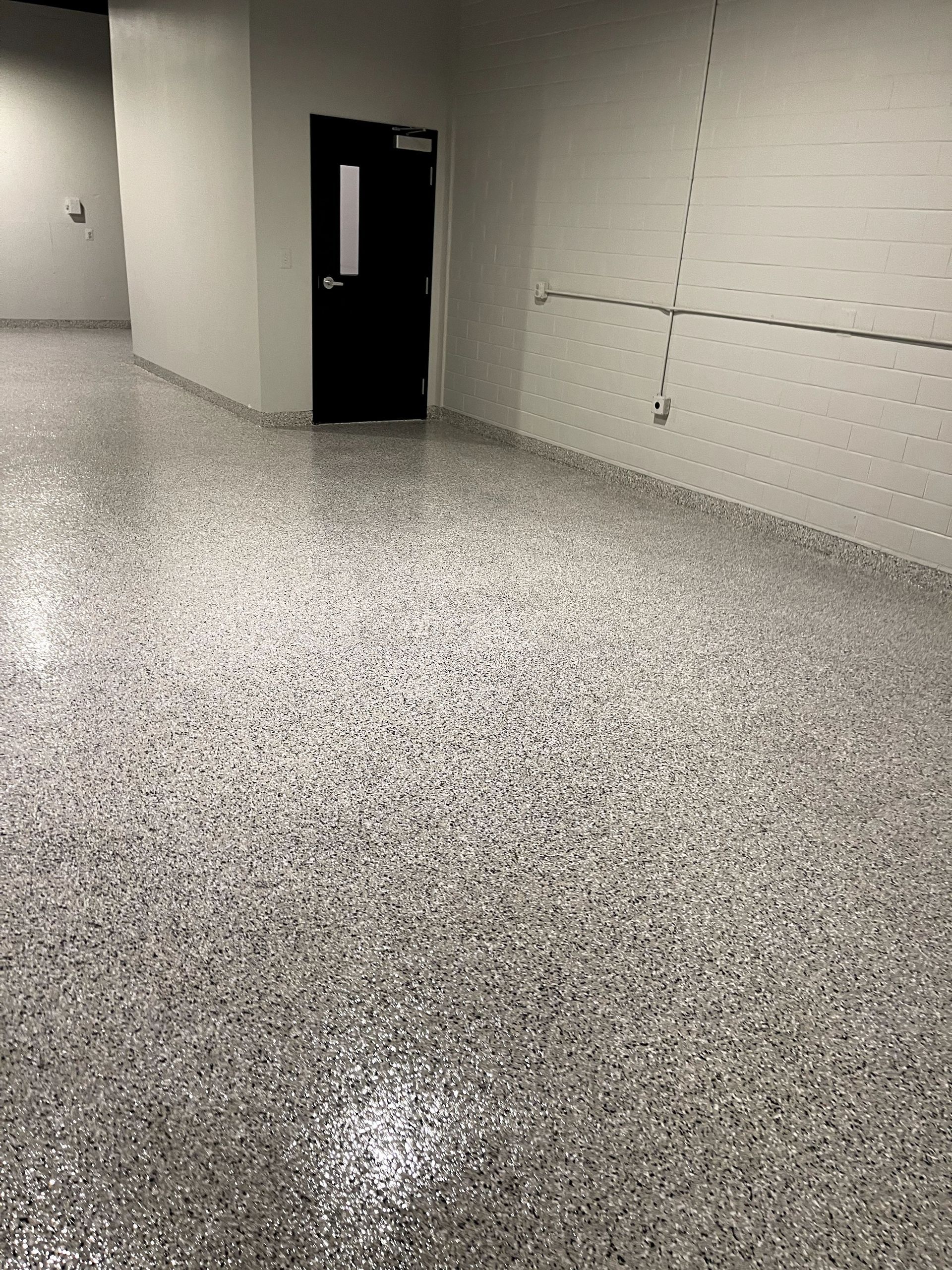 Empty hallway with speckled floor, white walls, and a dark open door ahead