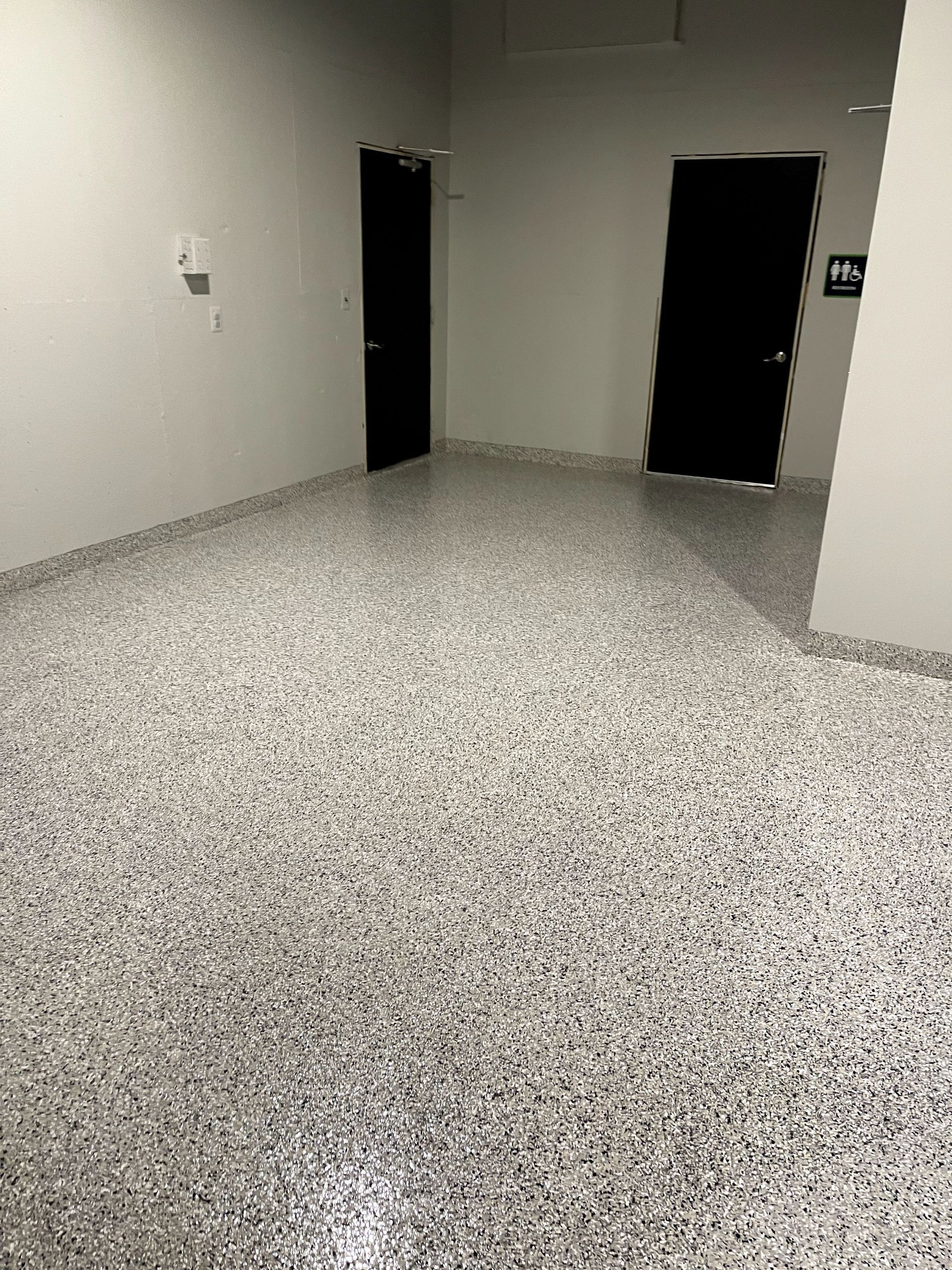 Empty gray room with speckled floor and two open black doorways.