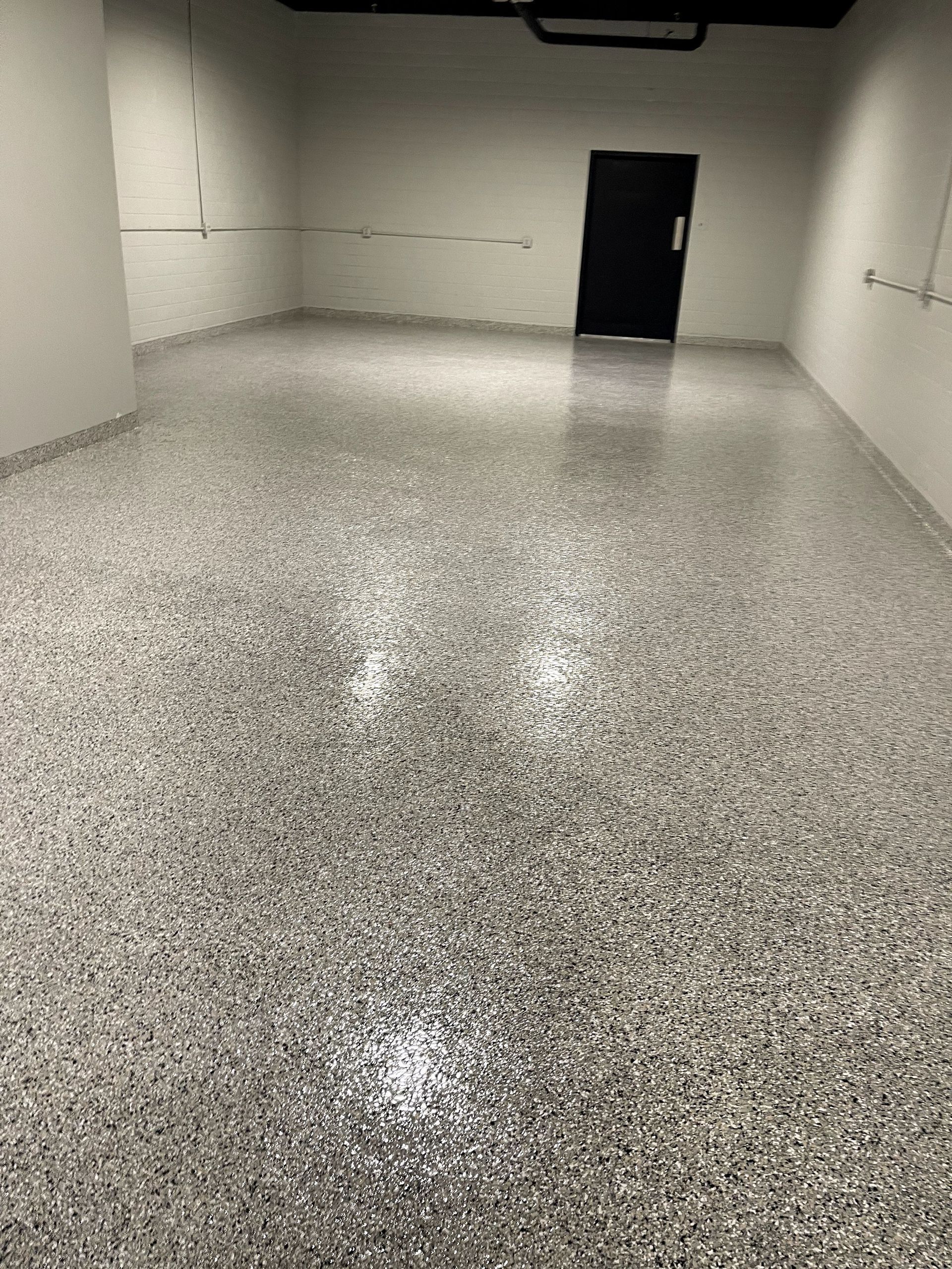 Empty speckled-floor room with white walls and a black door at the back