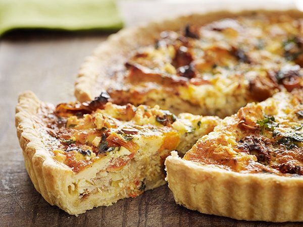 A quiche with a slice taken out of it on a wooden table.