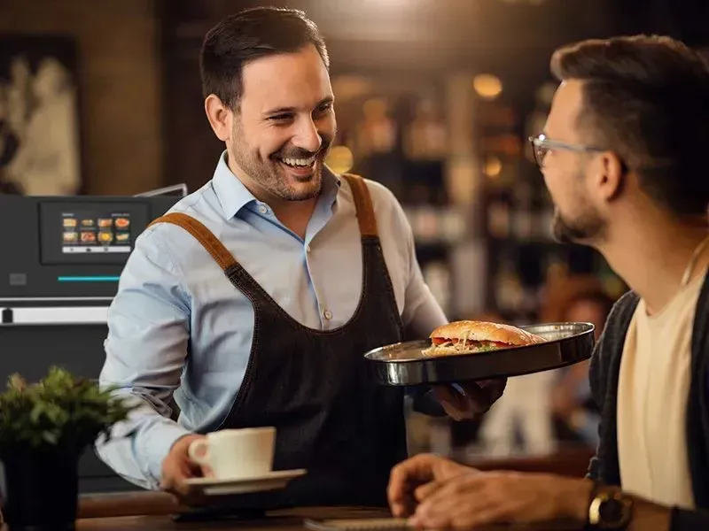A man is serving a hamburger to another man in a restaurant.