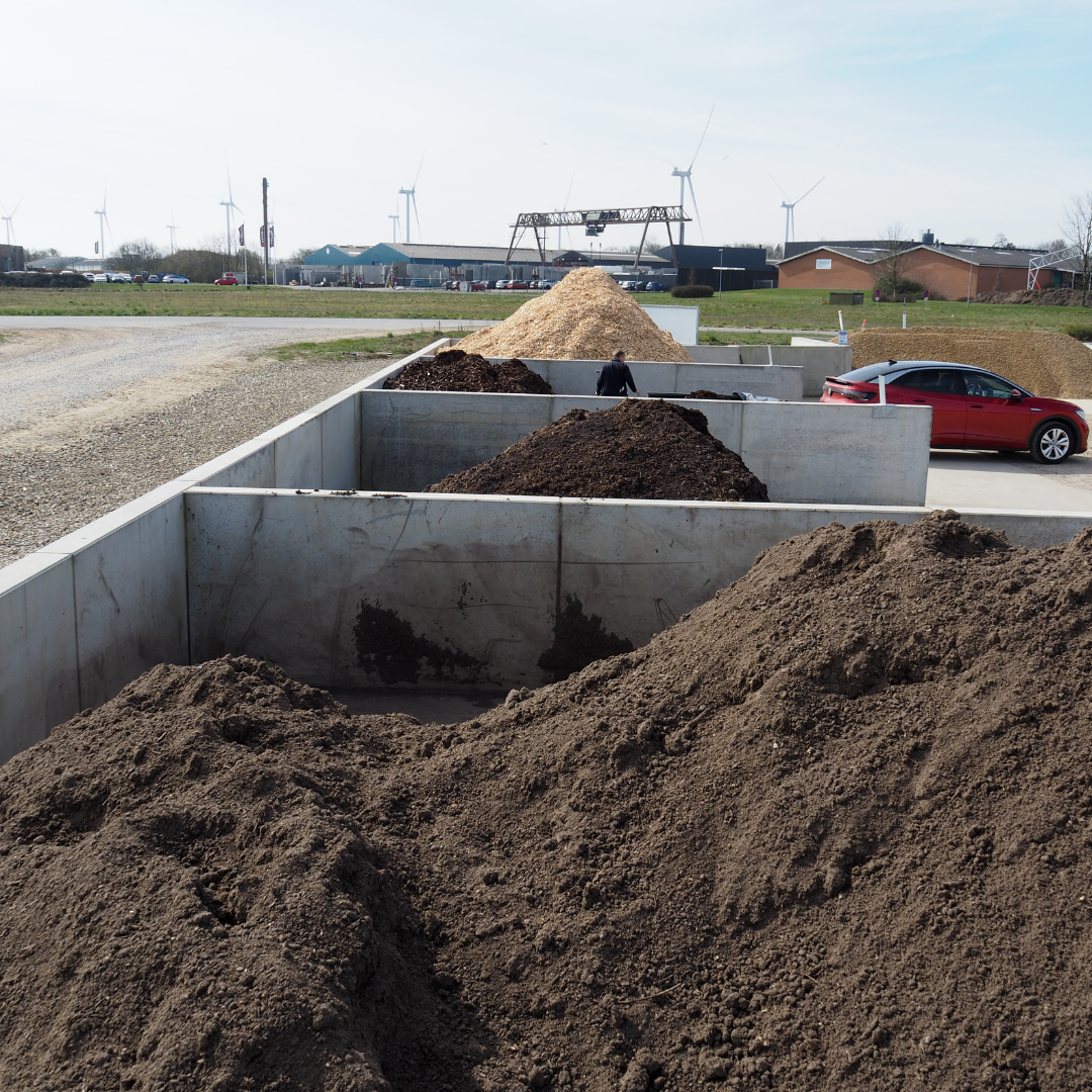 En sølvfarvet trailer ved siden af en bunke sand med en betonvæg i baggrunden på en udendørs byggeplads.