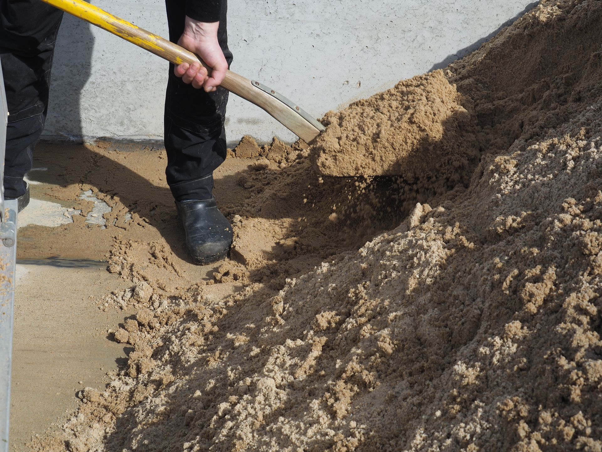 Person skovler sand ved siden af ​​en betonvæg.