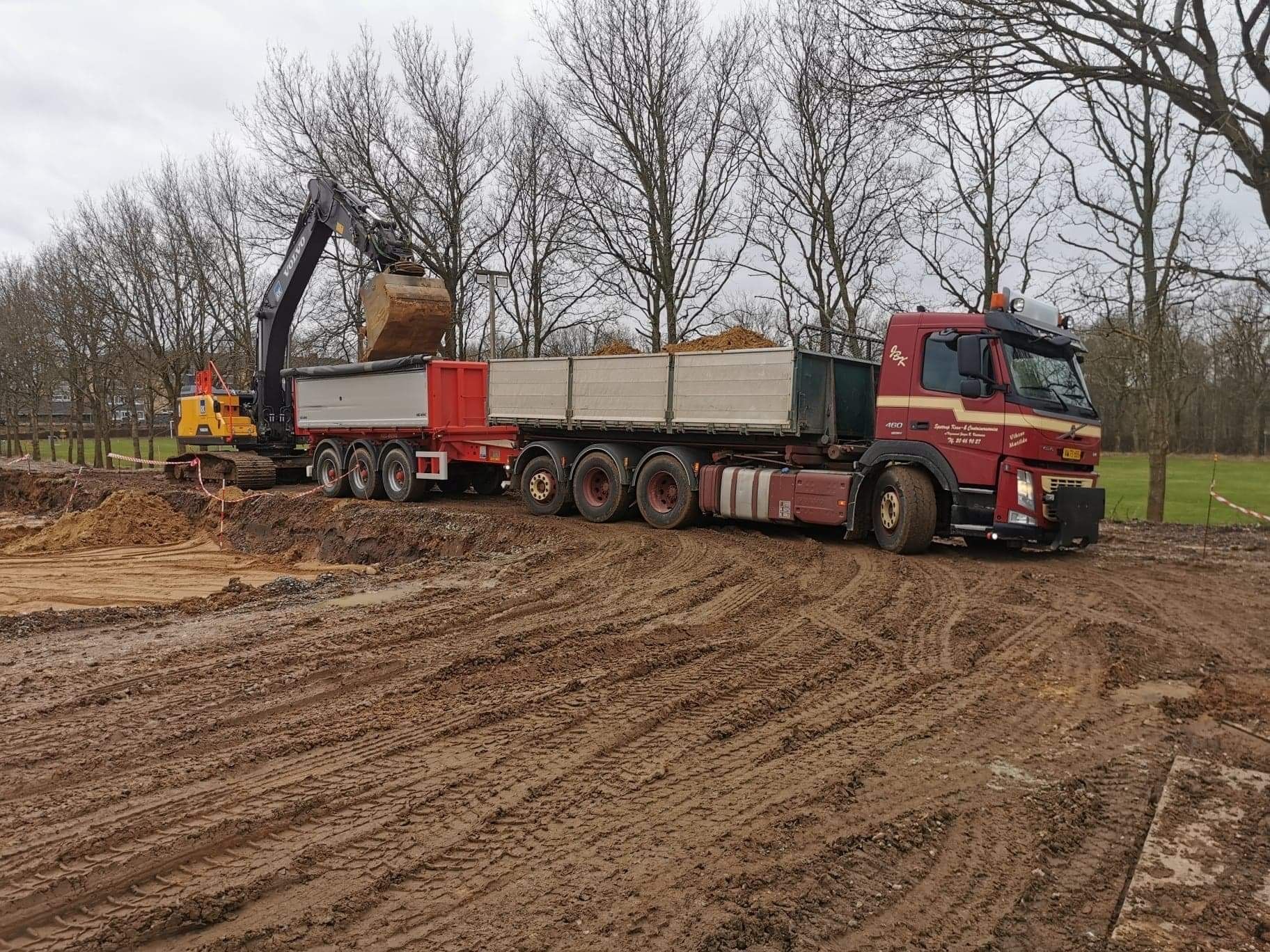 En rød trailer tømmer materiale på et grønt transportbånd; en person overvåger processen.