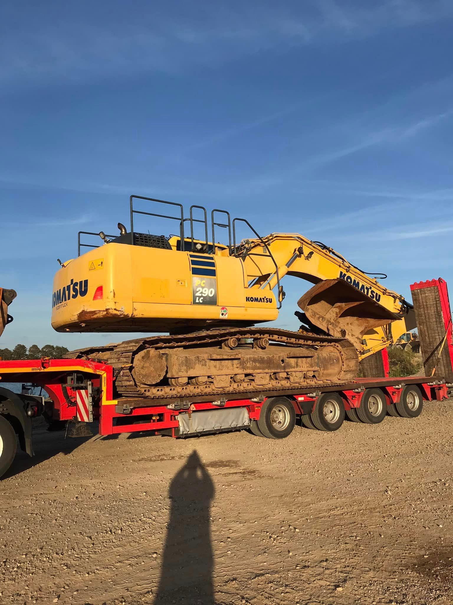 En rød trailer tømmer materiale på et grønt transportbånd; en person overvåger processen.