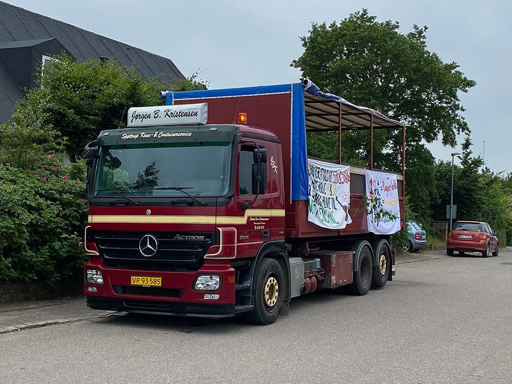 En rød trailer tømmer materiale på et grønt transportbånd; en person overvåger processen.