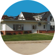 White house with a dark roof, brick foundation, and green lawn on a suburban street