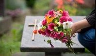 Person placing a colorful bouquet on a grave marker outdoors