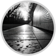 Black-and-white low-angle view of a wet sidewalk beside a wall of engraved text at dusk