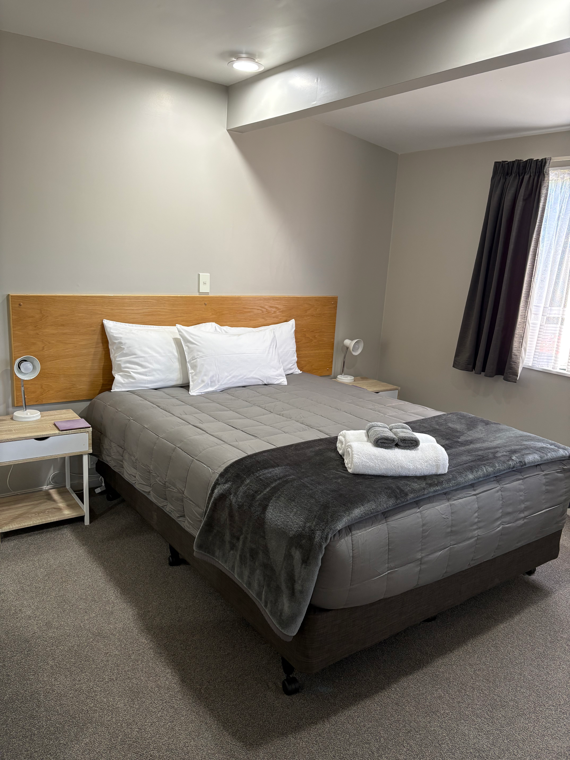 Hotel bedroom with a made bed, gray bedding, and a window with dark curtains